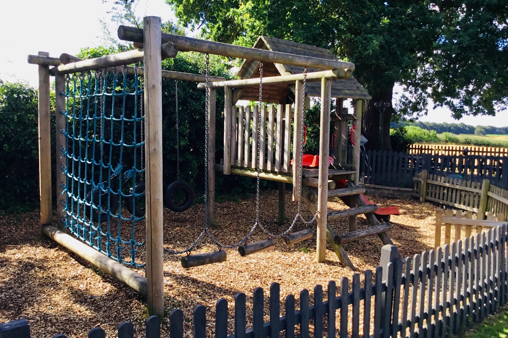 Children's playground with climbing ropes, slide, moving logs and a secure fence at The Stag Pub and Kitchen in Flackwell Heath.