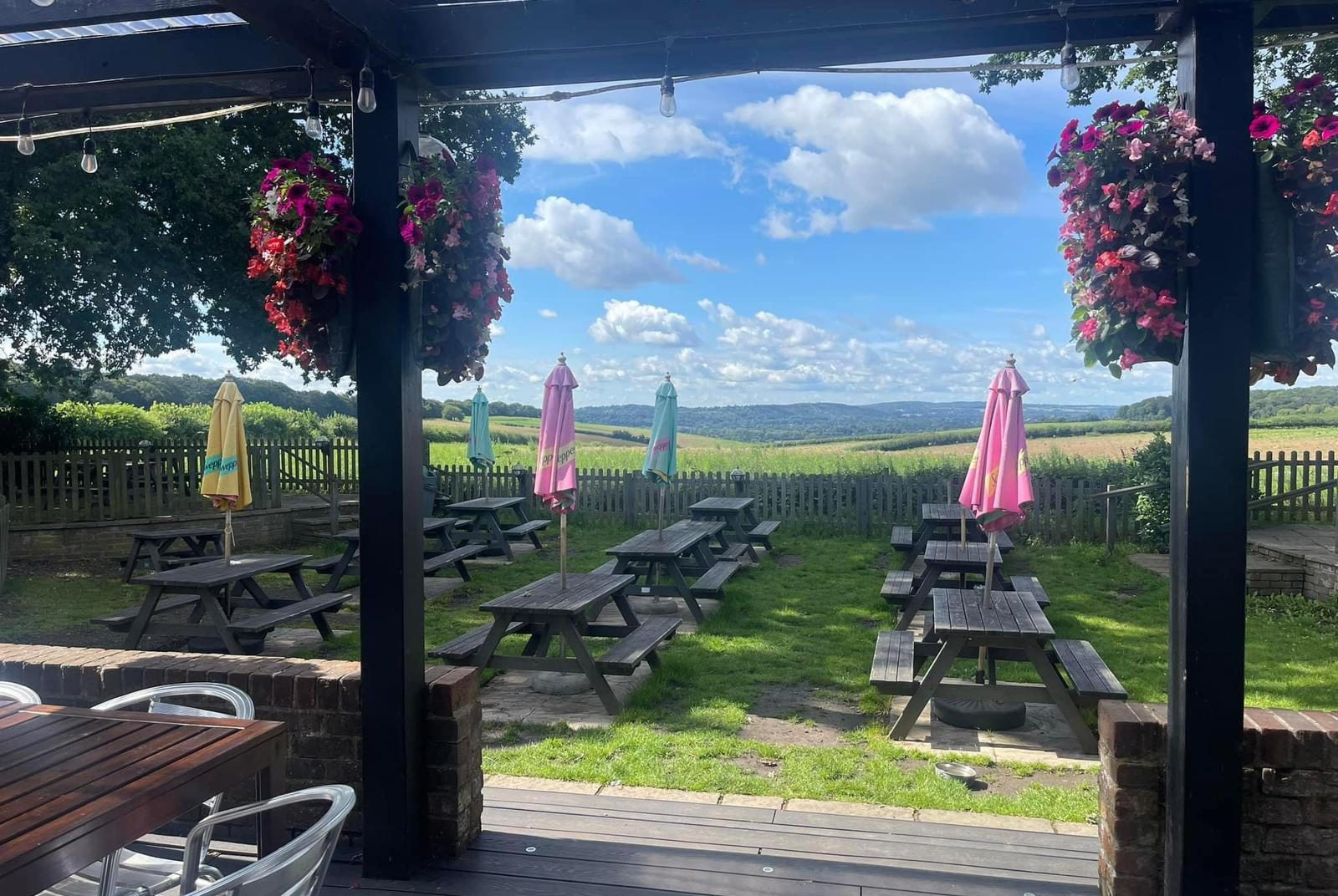 View of blue sky with white clouds, picnic tables with umbrellas, from the garden at The Stag Pub and Kitchen in Flackwell Heath.